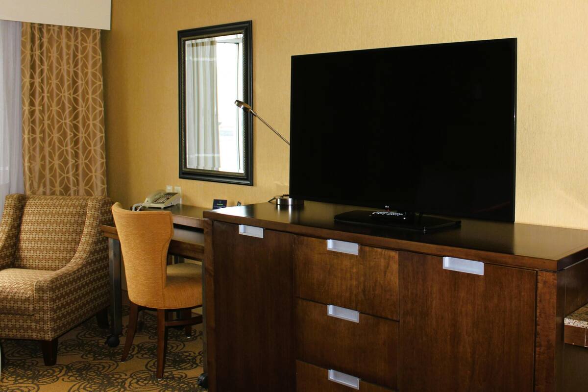 Une chambre d’hôtel avec un bureau en bois, une chaise, un téléviseur et une fenêtre avec des rideaux.
