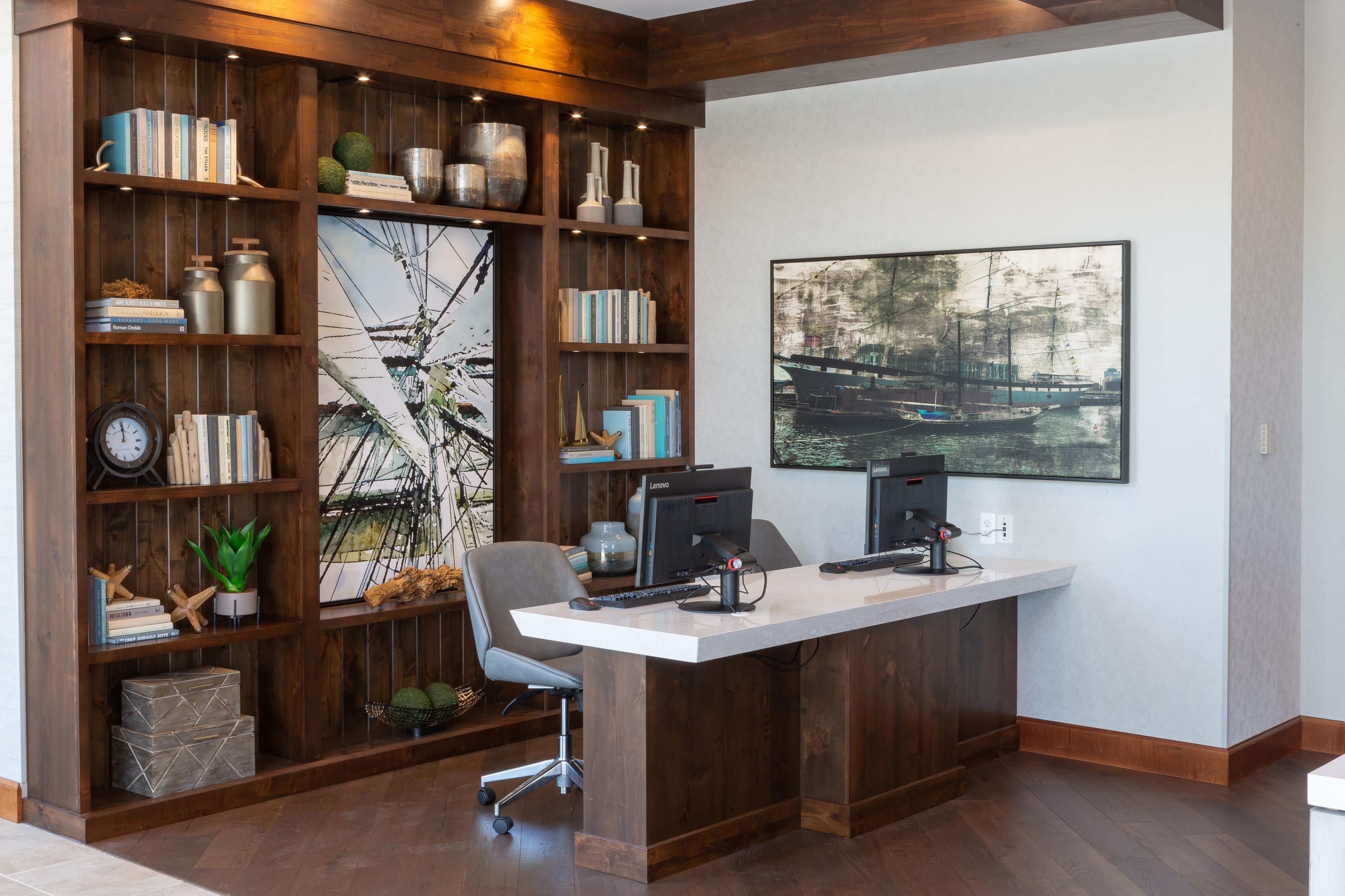 A home office with a desk, two monitors, a chair, and a bookshelf filled with books and decorative items.