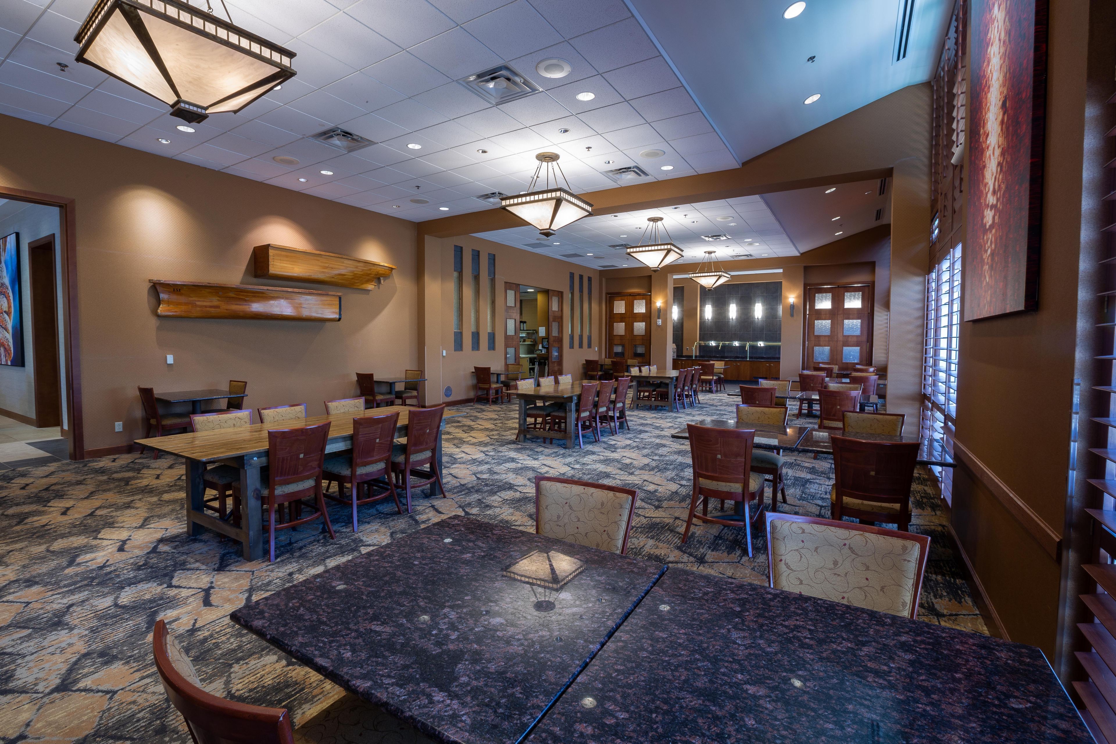 A hotel conference room with multiple tables and chairs, a patterned carpet, and a high ceiling with recessed lighting.