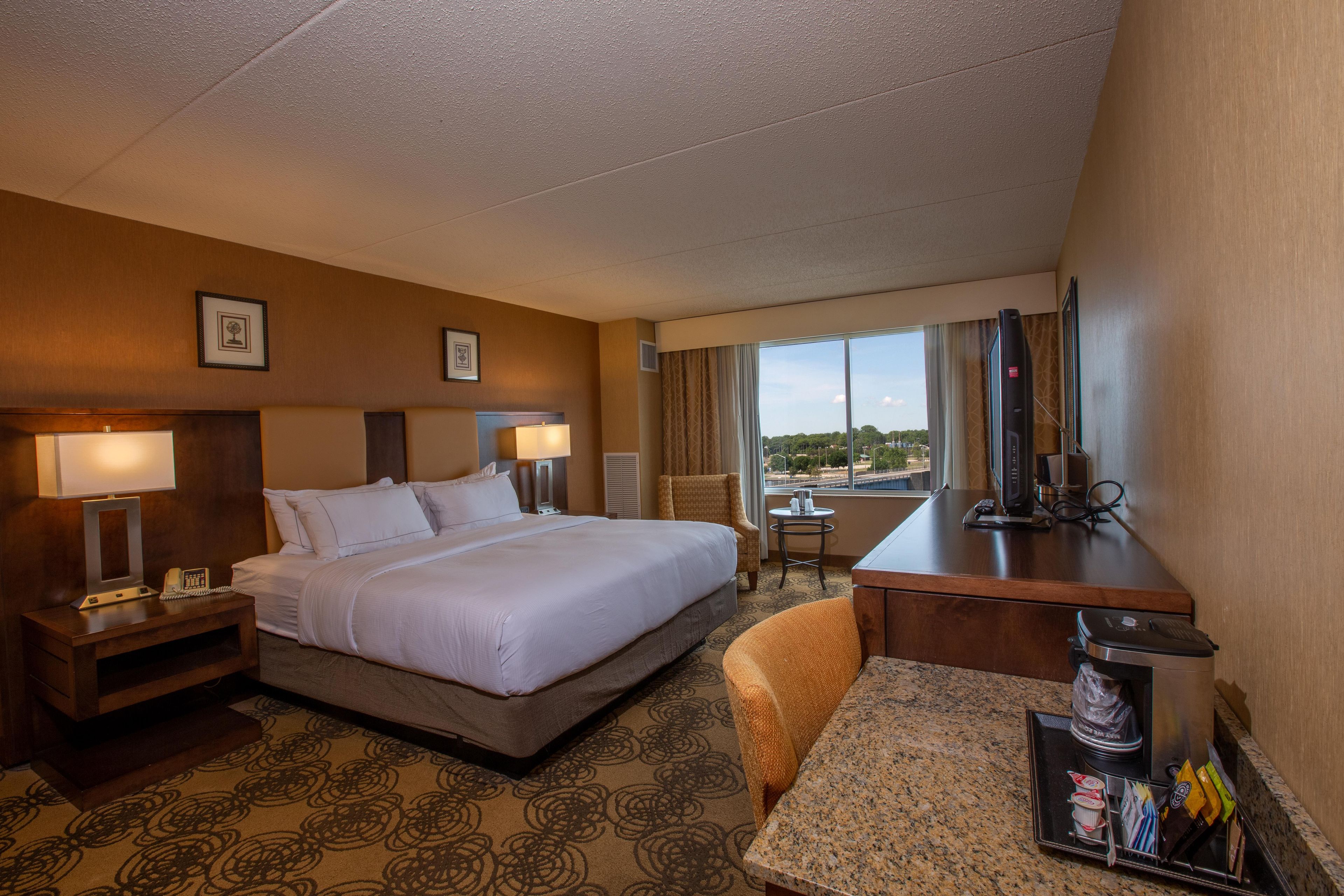 A hotel room with a bed, bedside tables, a desk, a chair, a television, and a window with a view.