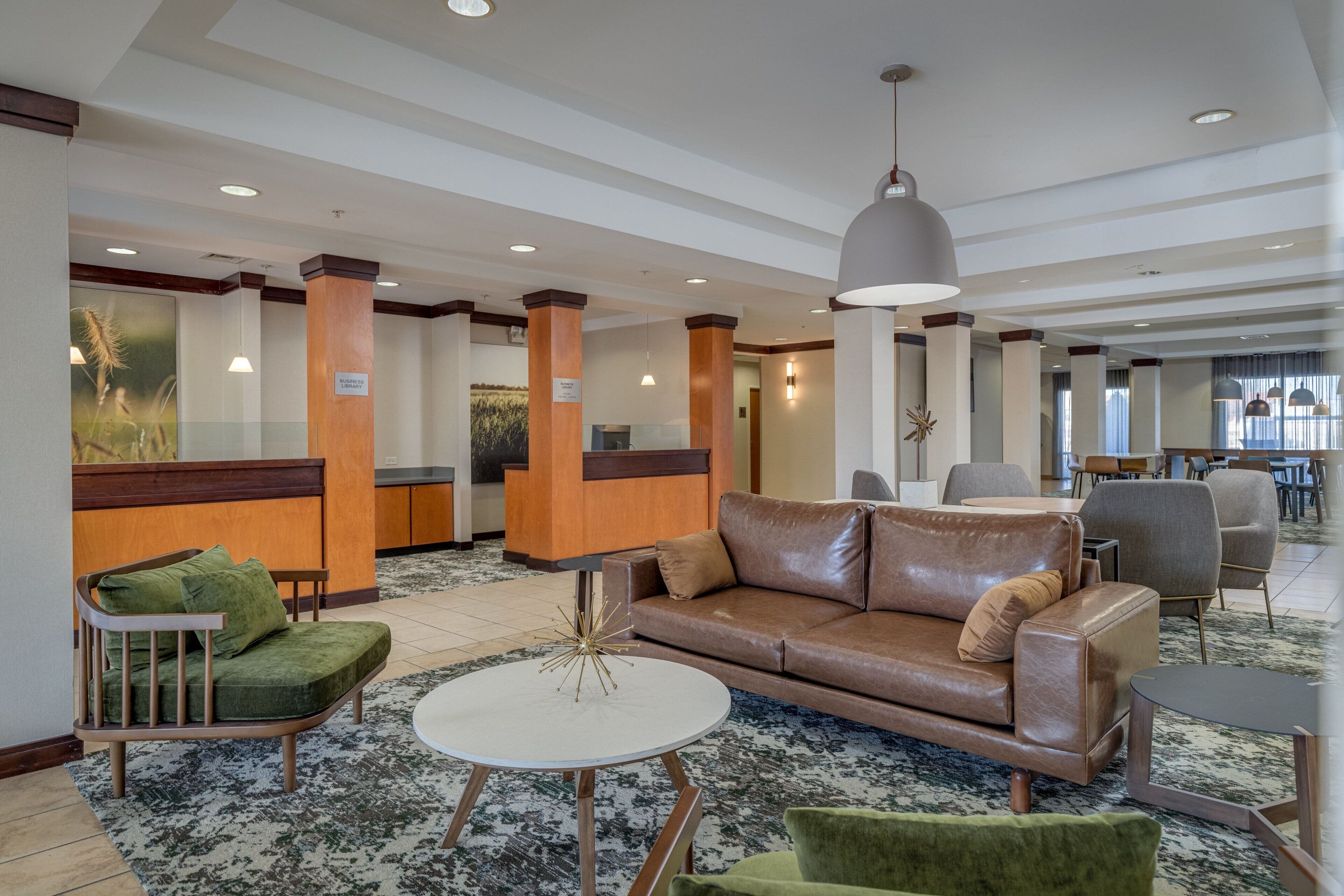 A lobby with a brown leather sofa, green armchairs, a white coffee table, and a reception desk.