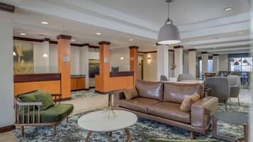 A lobby with a brown leather sofa, green armchairs, a white coffee table, and a reception desk.