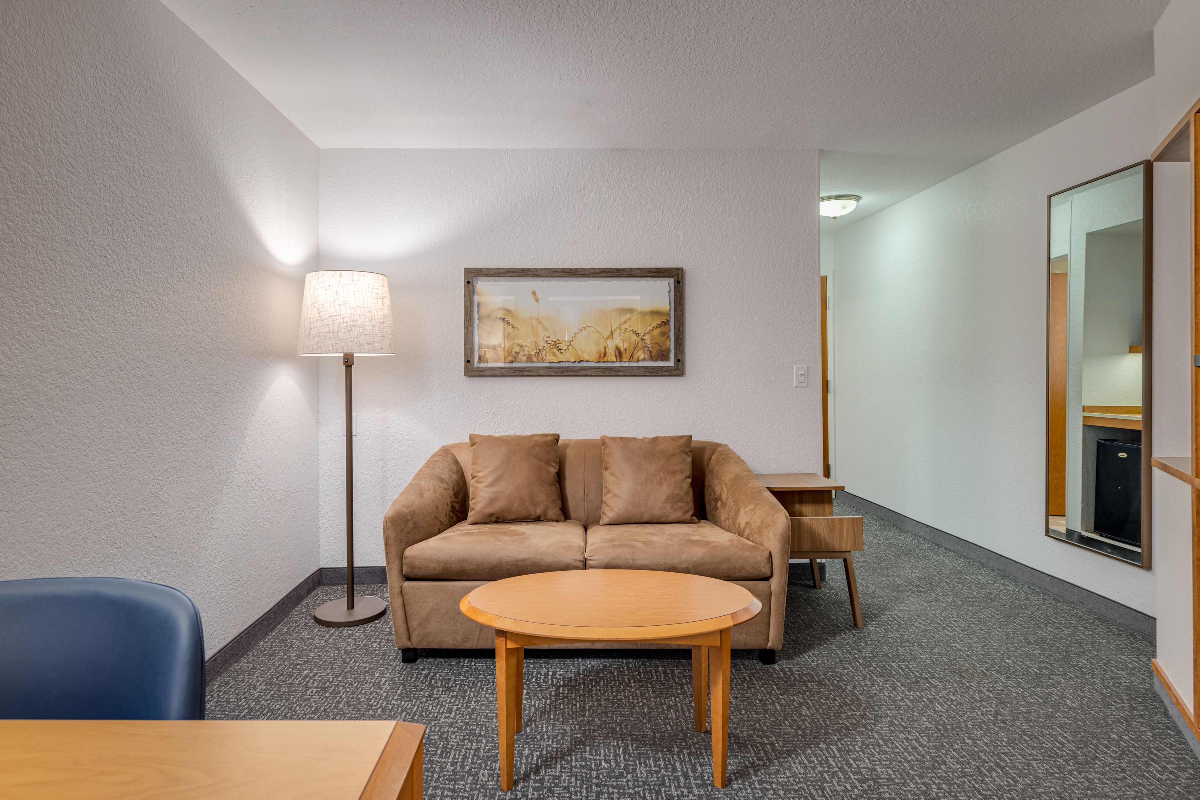 Une chambre d’hôtel avec un canapé, une table ronde, une lampe sur pied, un tableau encadré au mur et un miroir au mur.