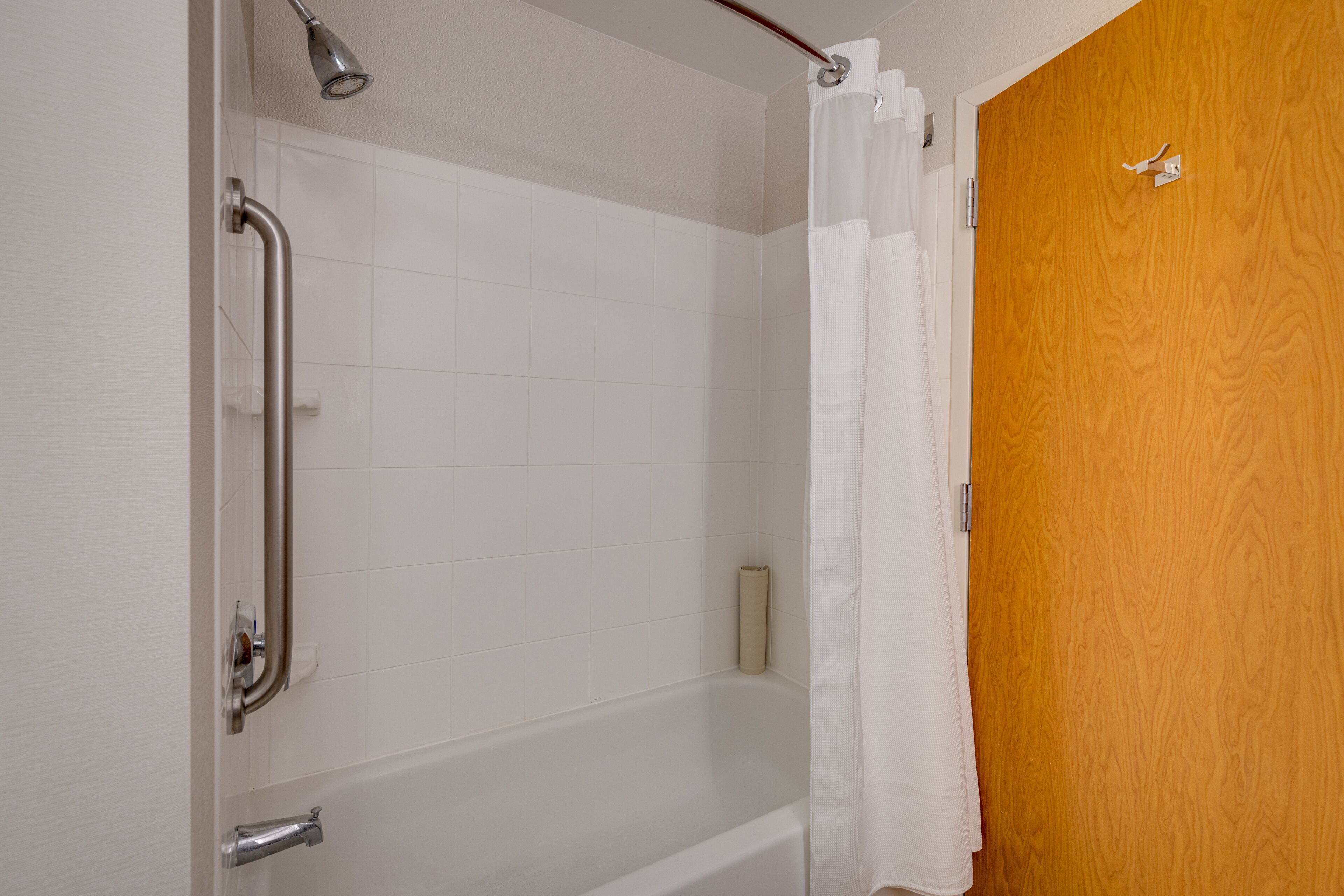 Ein Badezimmer mit einer weißen Badewanne, einer Holztür und einer Dusche mit Vorhang.