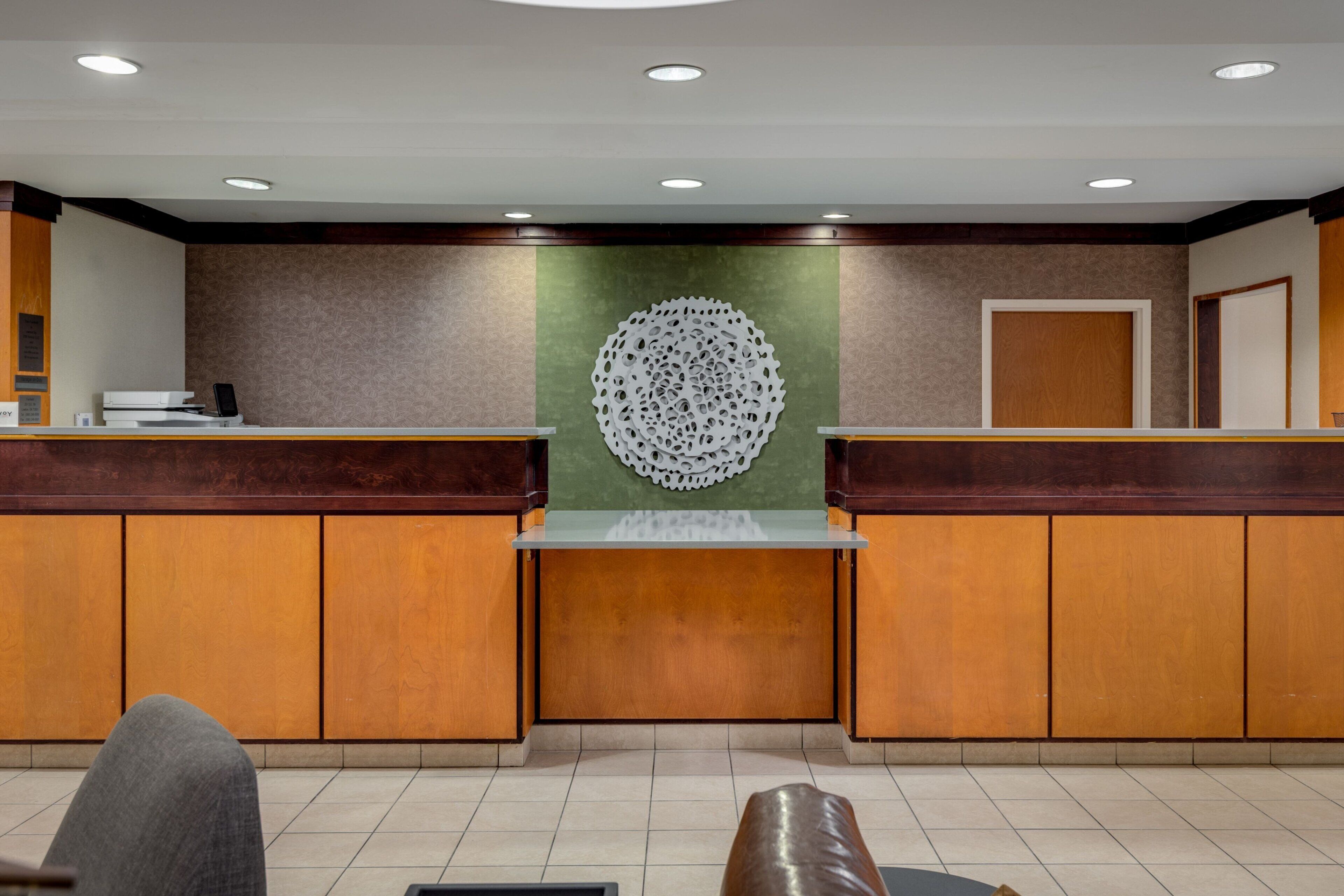 Un área de recepción con un mostrador de madera, una pared de acento verde y una pieza decorativa circular en la pared.