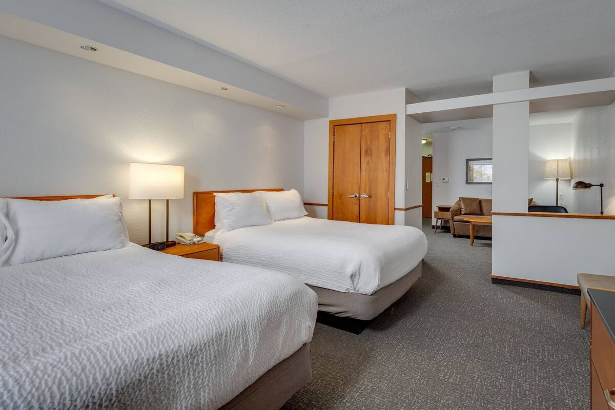 Une chambre d’hôtel avec deux lits, un bureau, une chaise et une armoire.