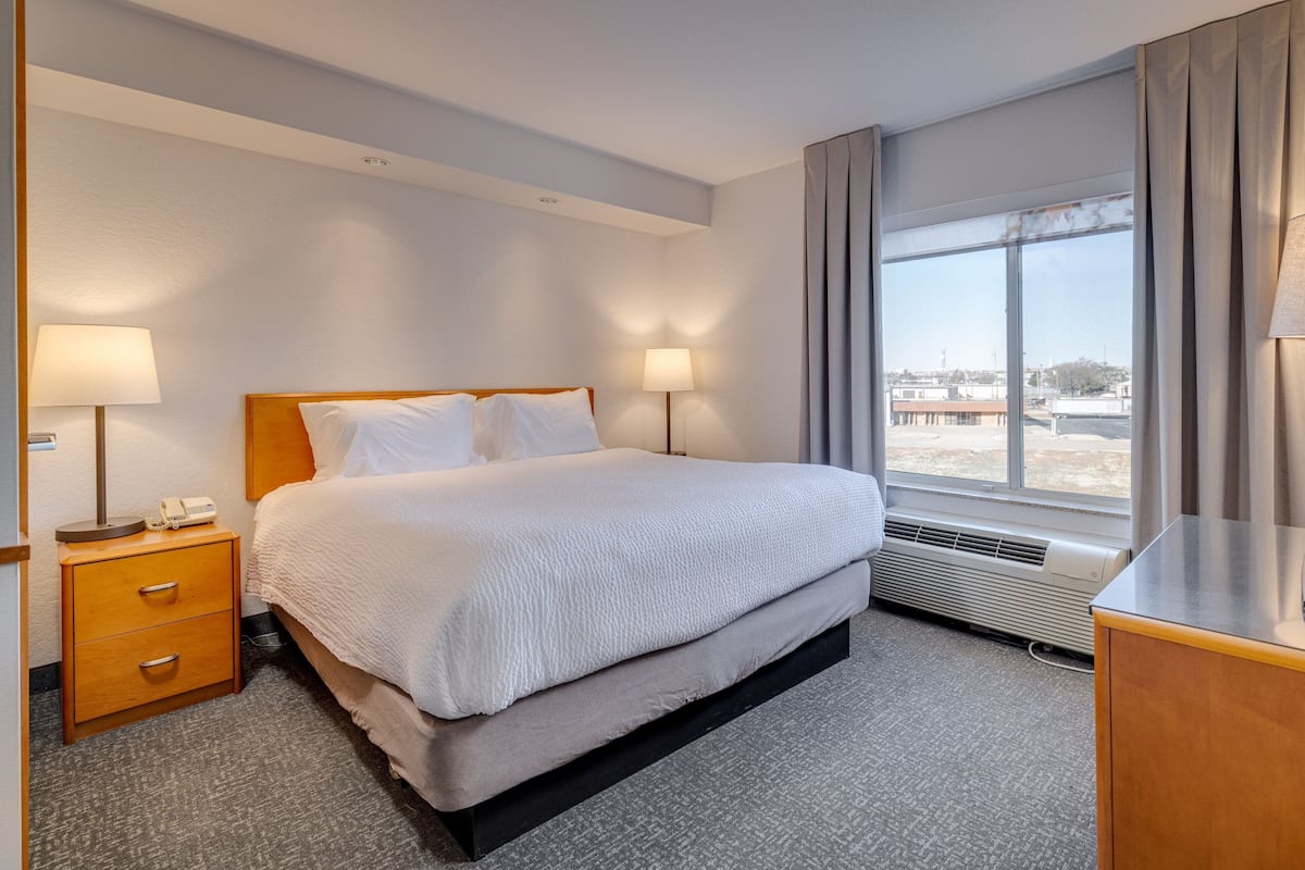 Une chambre d’hôtel comprenant un lit, des lampes de chevet, une table de chevet, un bureau et une fenêtre donnant sur des immeubles.