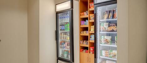 A vending machine area with a refrigerator stocked with beverages and snacks, and a wooden cabinet with packaged food items.