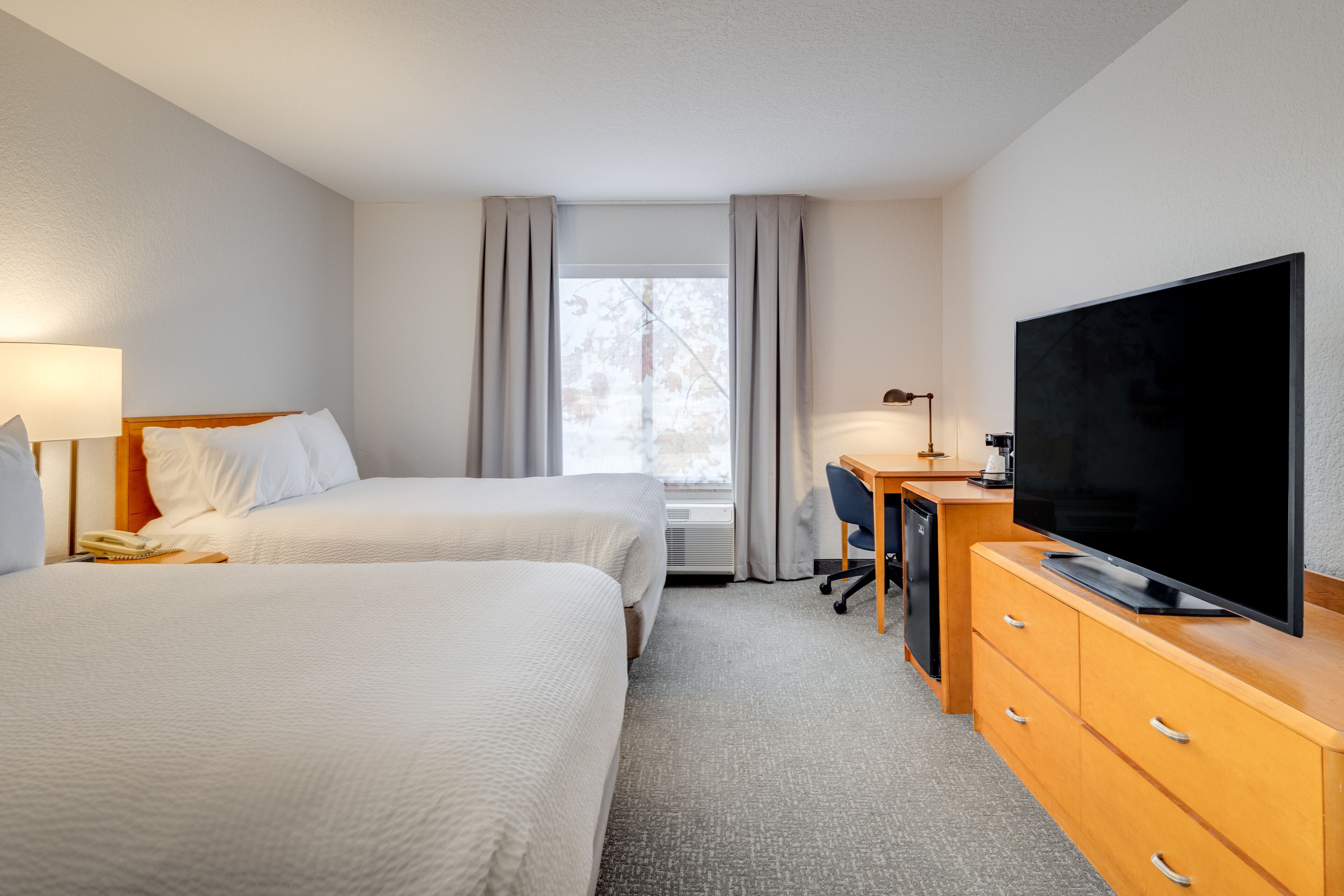 A hotel room with two beds, a desk, a television, and a window with curtains.