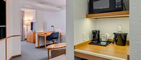 A compact hotel room with a kitchenette, a desk, and a chair.