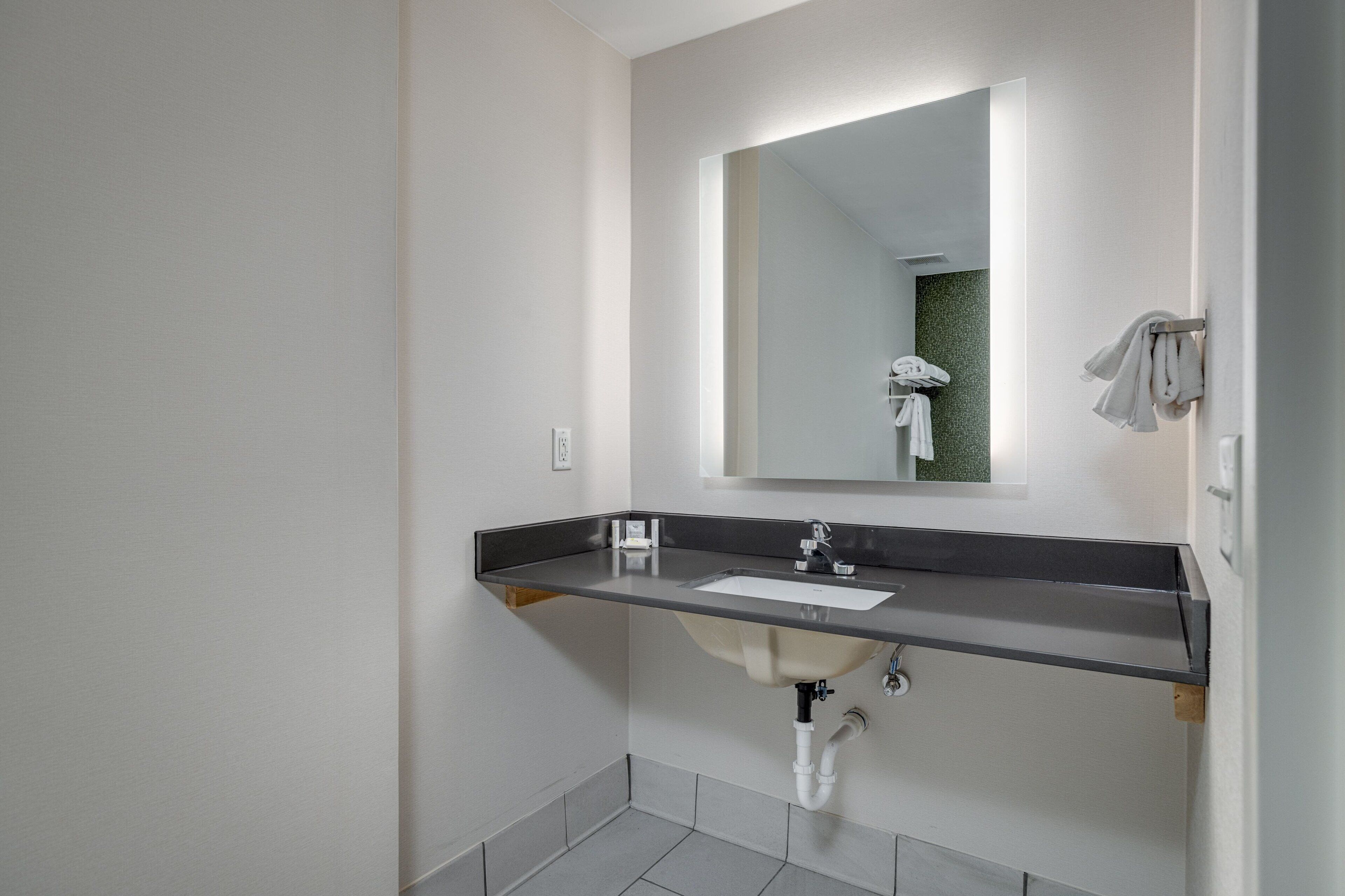 A modern bathroom with a dark countertop, a white sink, and a large mirror.