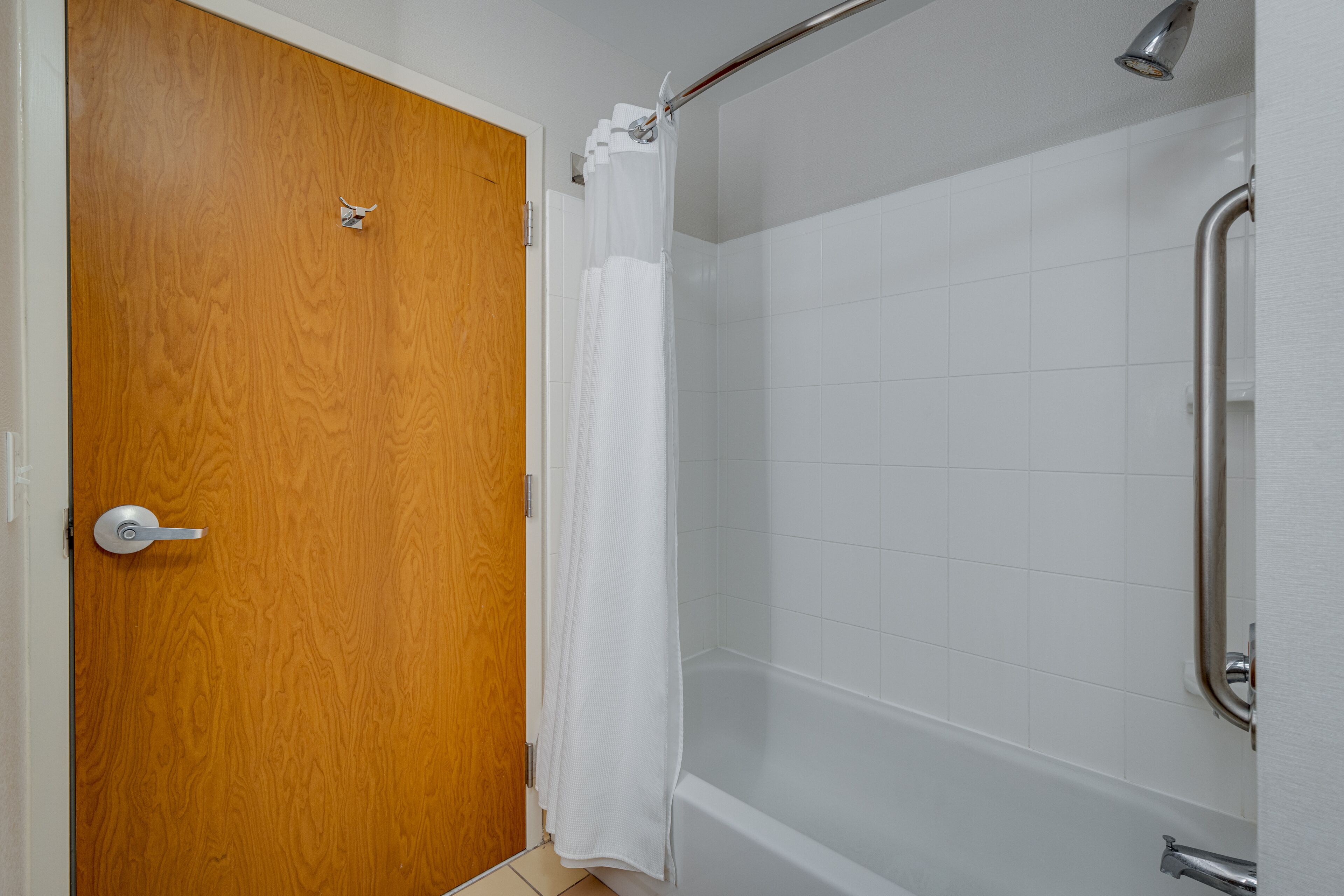 Une porte en bois, un rideau de douche blanc et une cabine de douche carrelée de blanc.
