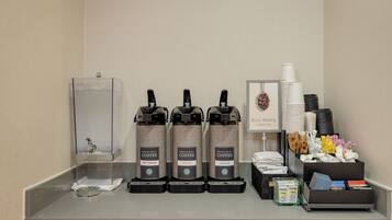 A coffee station with three coffee dispensers labeled "Premium Select Coffee" and "Hot Water," a water dispenser, and a stack of white cups.