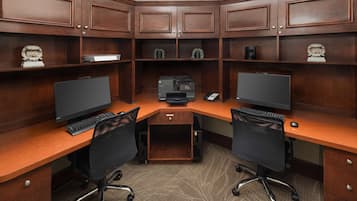 A corner office with two desks, each with a computer, keyboard, and chair. There are shelves above the desks with decorative items and a printer in the center.