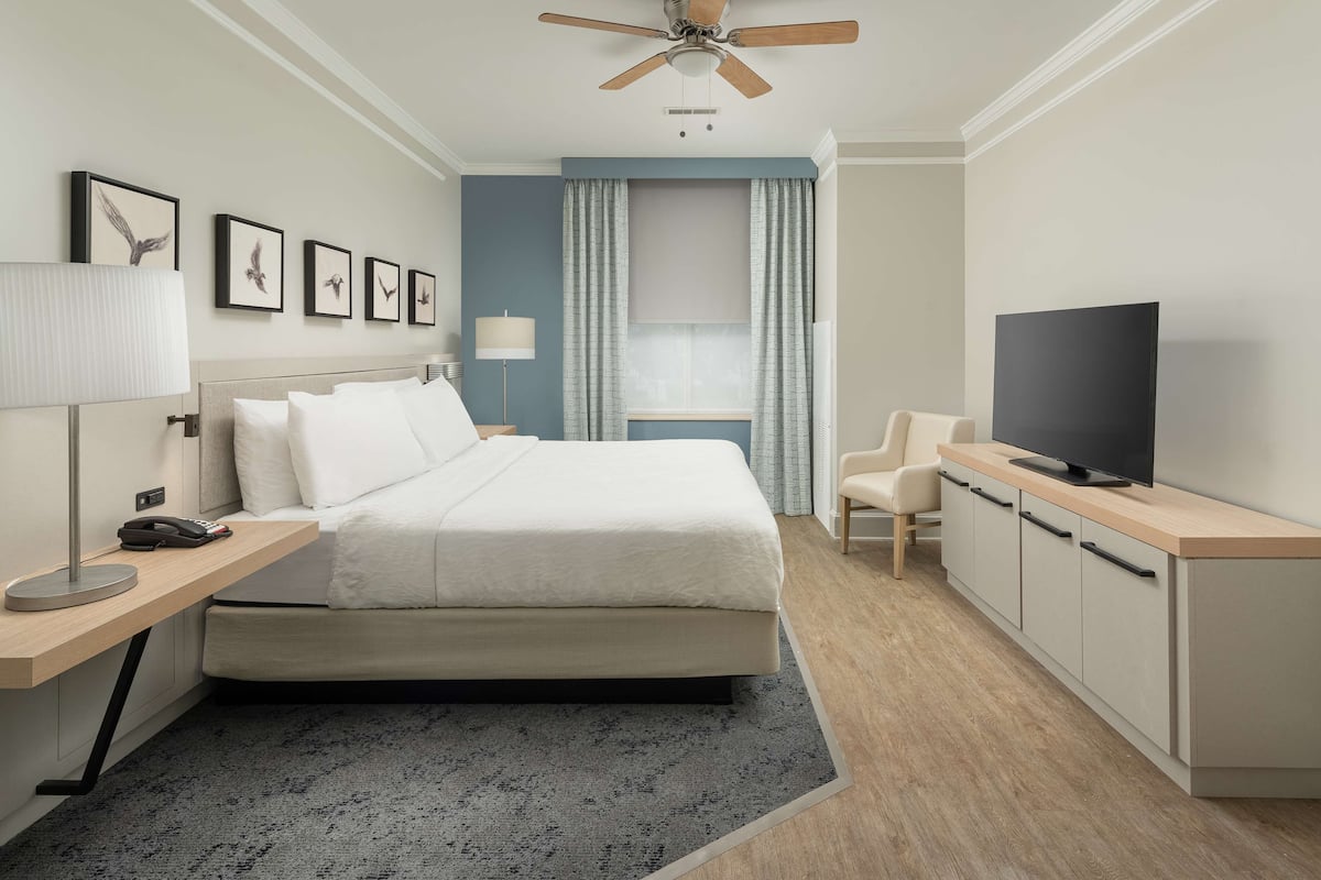 A hotel room with a bed, a desk with a lamp, a television, and a window with curtains.