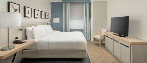 Una habitación de hotel con cama, escritorio con lámpara, televisor y ventana con cortinas.