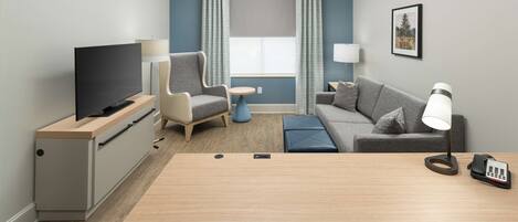 A modern hotel room with a flat-screen TV, a desk, a sofa, and a small round table.