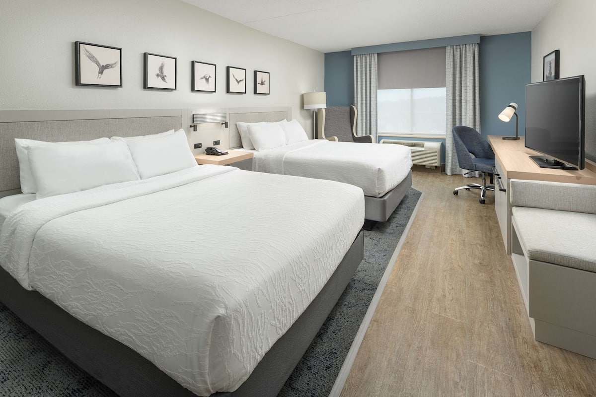 A hotel room with two beds, a desk with a TV, a chair, and framed pictures on the wall.
