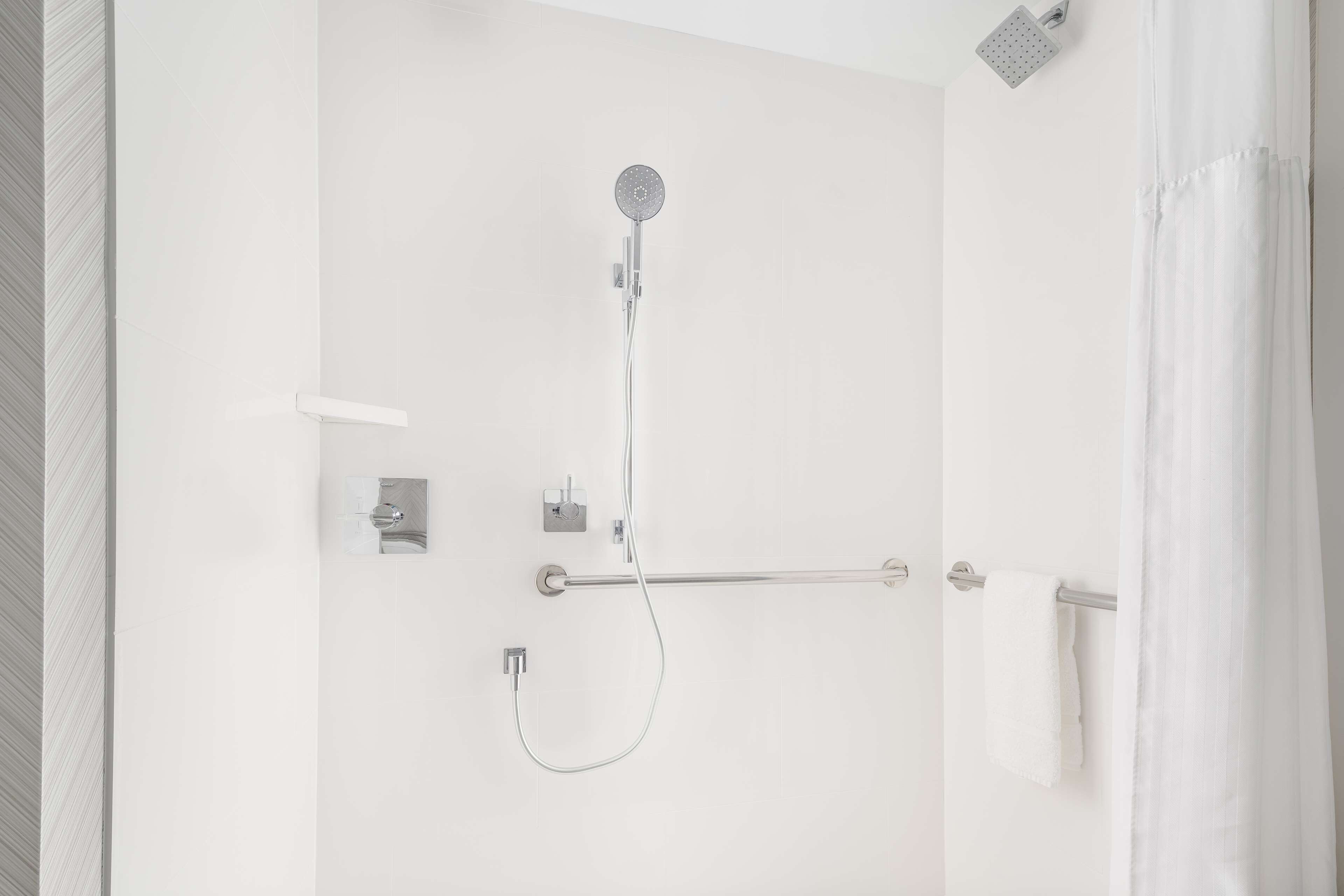 A modern shower with a handheld showerhead, a towel bar, and a towel hanging on the wall.