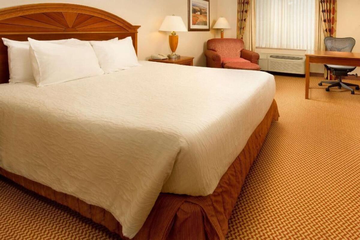 A hotel room with a large bed, a desk, a chair, a lamp, and a picture on the wall.