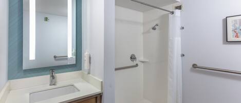 A modern bathroom with a sink, mirror, shower, and handrails.