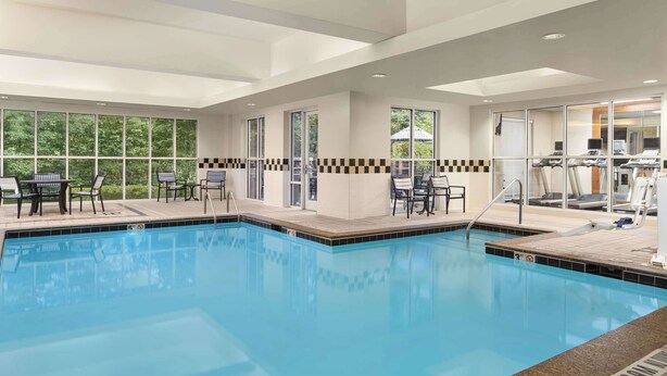 Ein heller, überdachter Pool mit klarem, blauem Wasser, umgeben von Liegestühlen und Tischen.