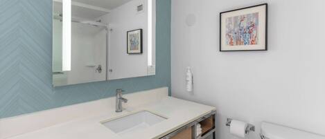 A modern bathroom with a white sink, a large mirror, and a framed abstract painting on the wall.