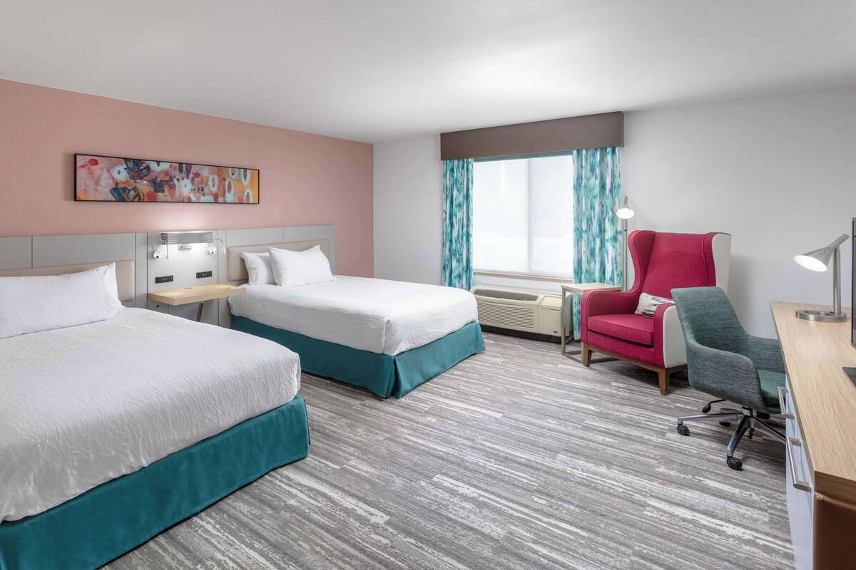 A hotel room with two beds, a desk, a chair, and a window with curtains.