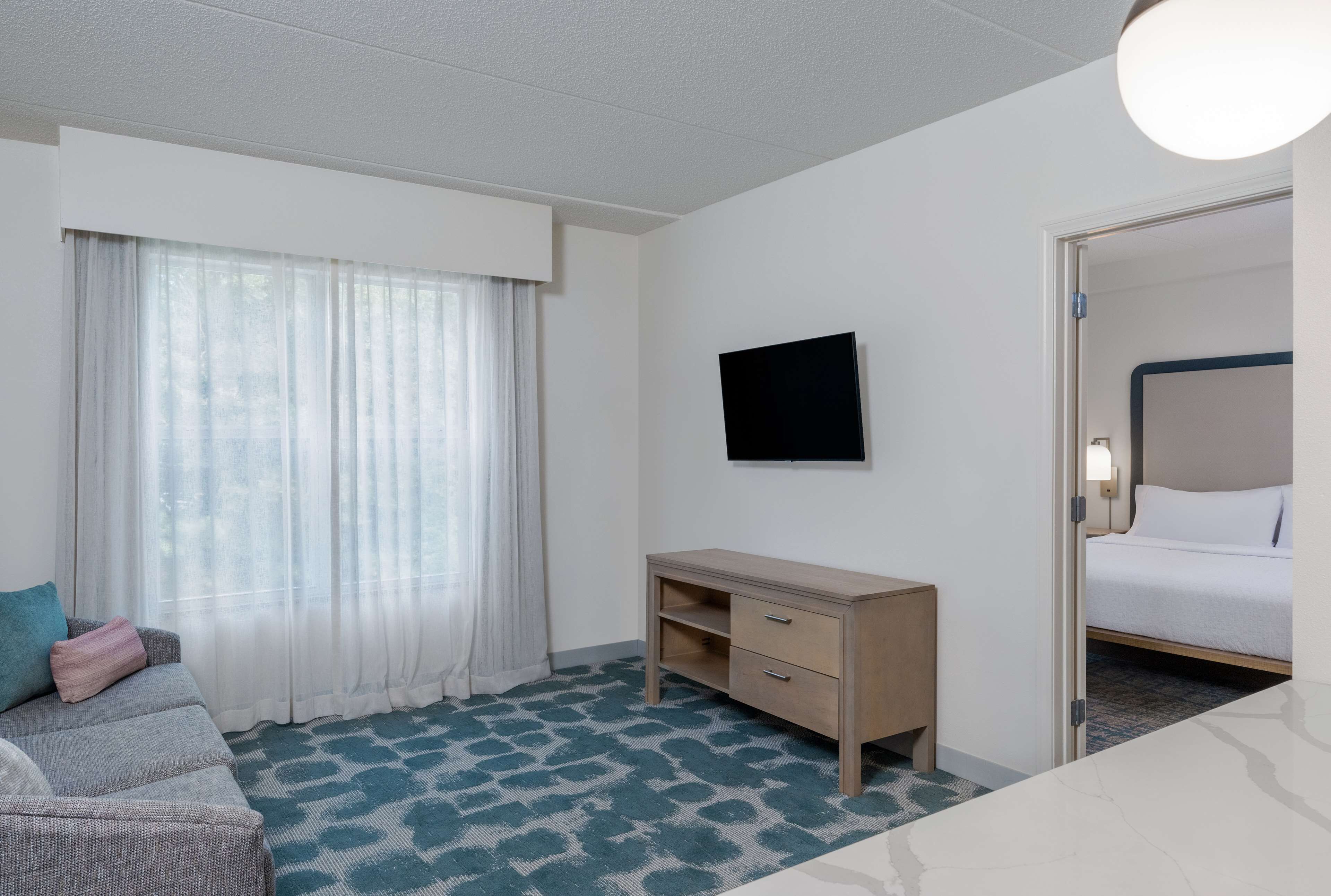 A hotel room with a bed, a desk, a television, and a window with curtains.