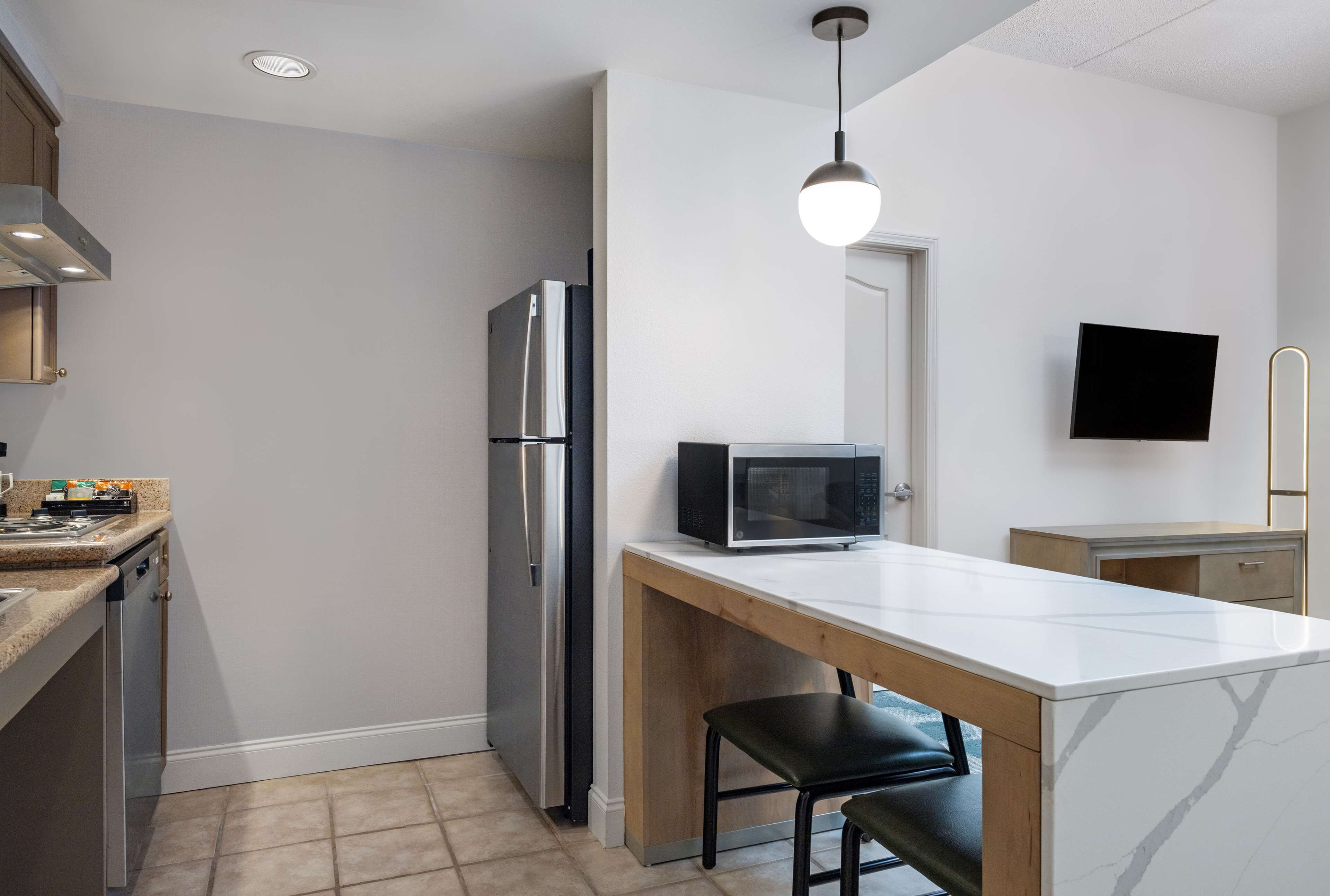 A compact kitchen with a refrigerator, microwave, and a small dining area with a chair.