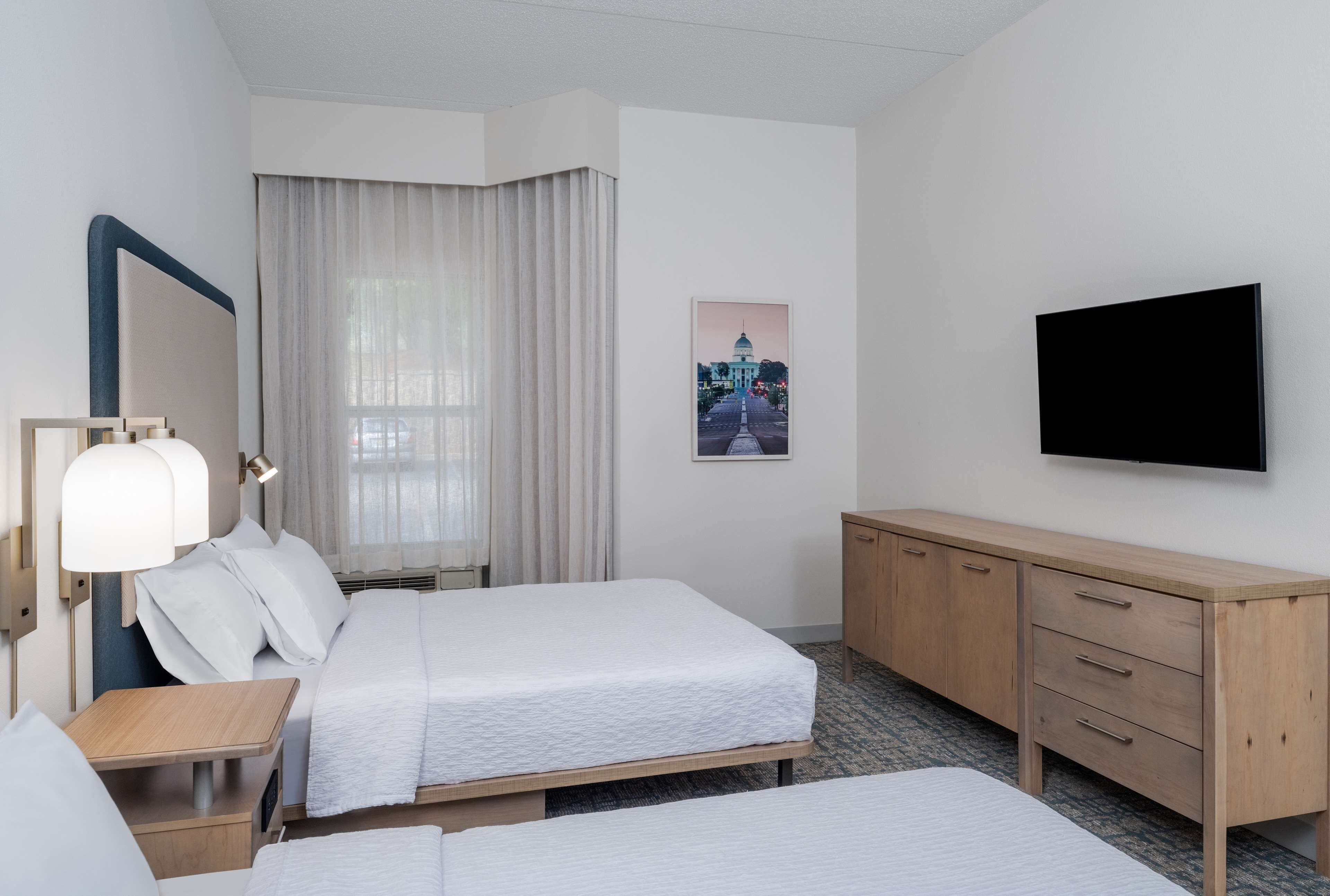 Een hotelkamer met twee bedden, een bureau, een spiegel, een televisie en een schilderij aan de muur.