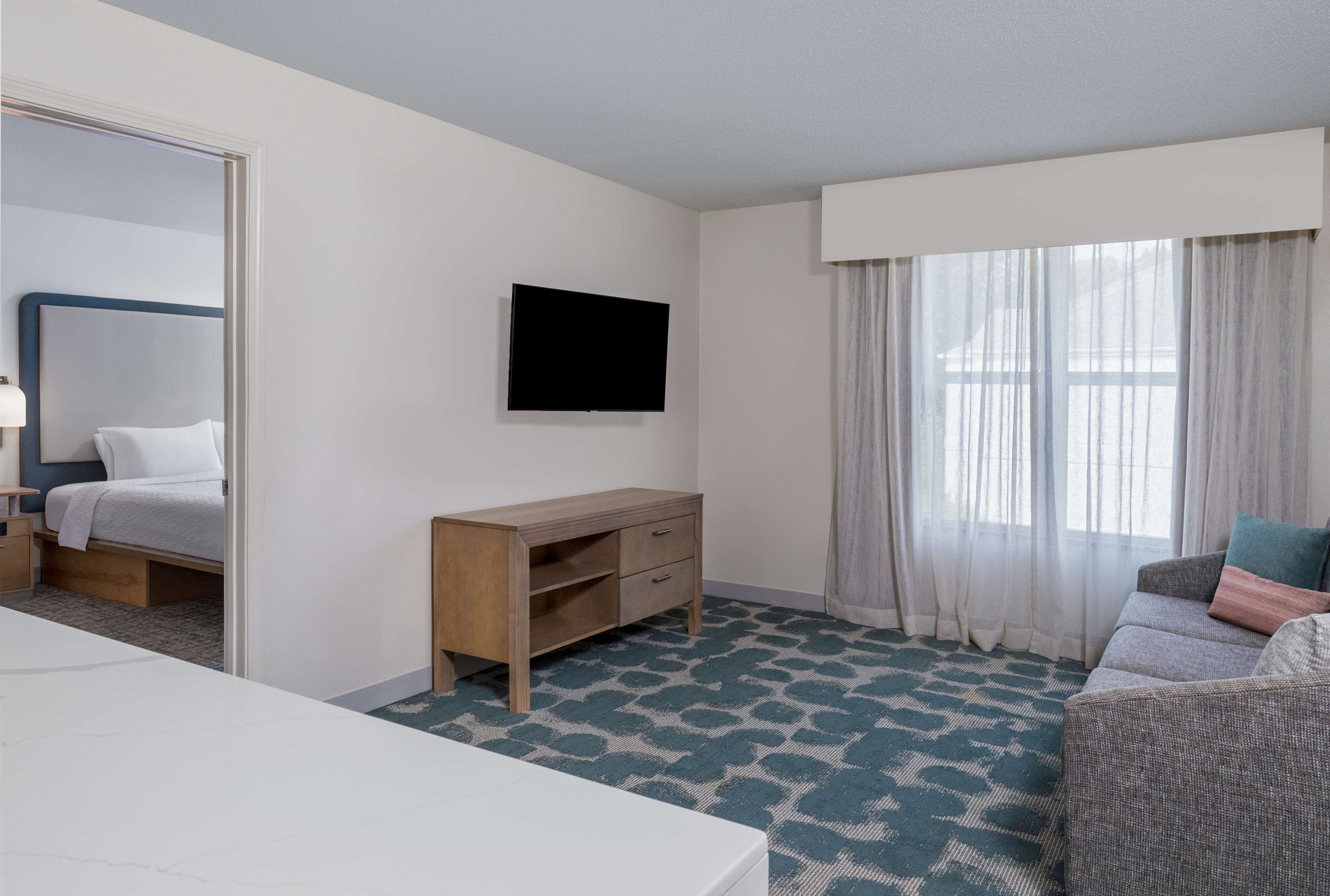 A hotel room with a bed, a desk, a television, a sofa, and a window with curtains.