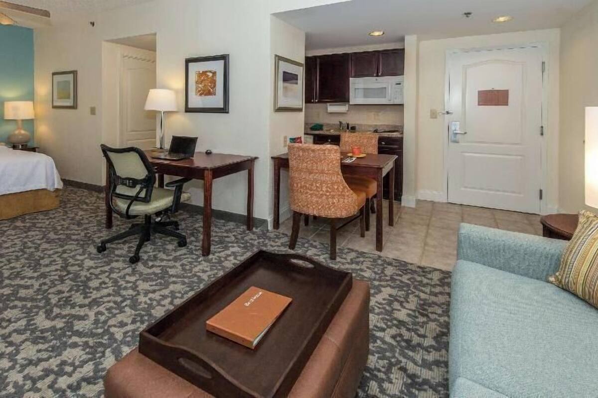 A hotel room with a bed, desk, office chair, dining table, and kitchenette.