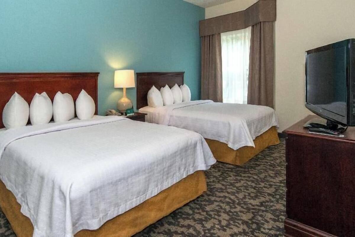 A hotel room with two beds, a television, and a lamp.