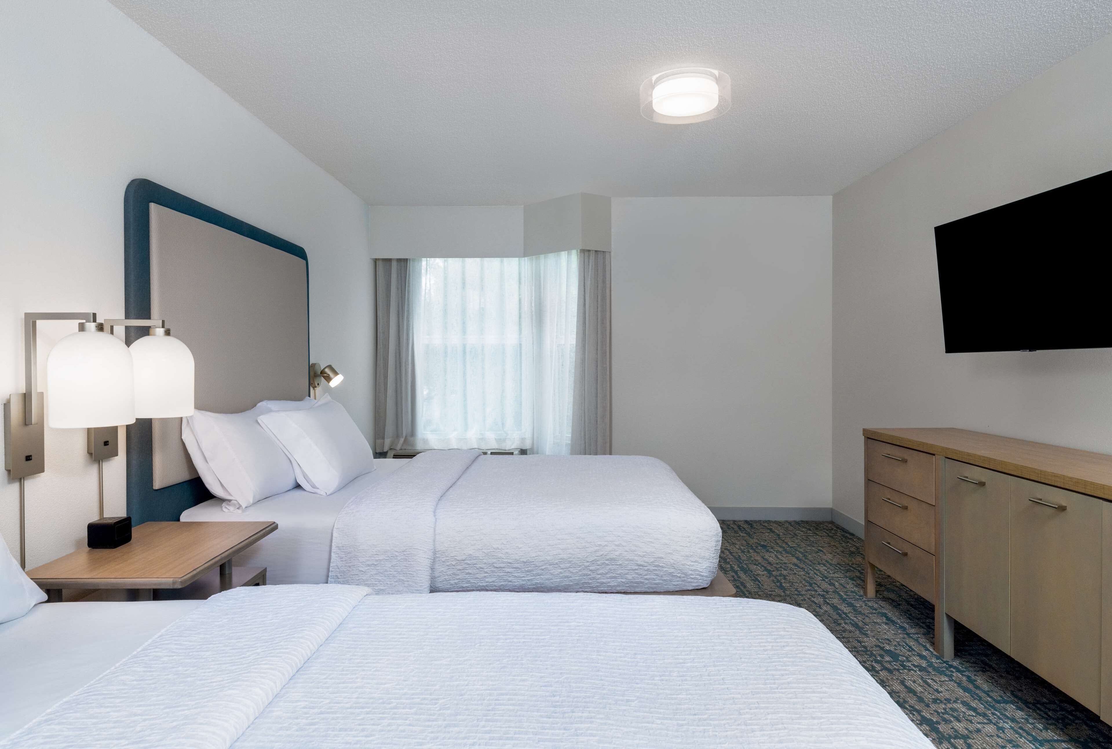 A hotel room with two beds, a desk, a TV, and a window with curtains.