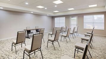 A conference room with a long table and several chairs arranged around it. The room has a carpeted floor and large windows on one side.