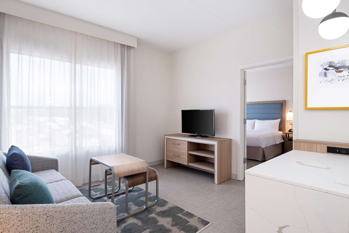 A hotel room with a sofa, a small table, a TV, a bed, and a bathroom.