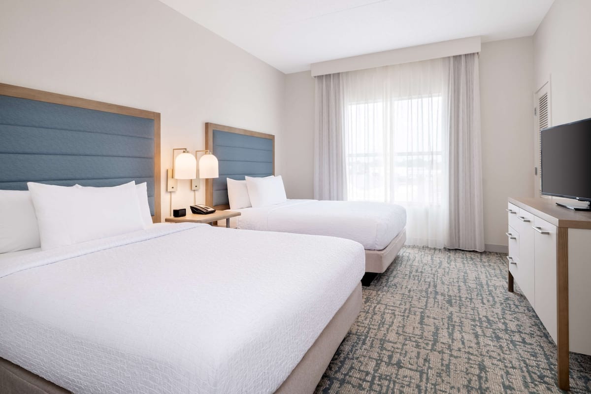 A hotel room with two beds, a desk, a television, and a window with curtains.