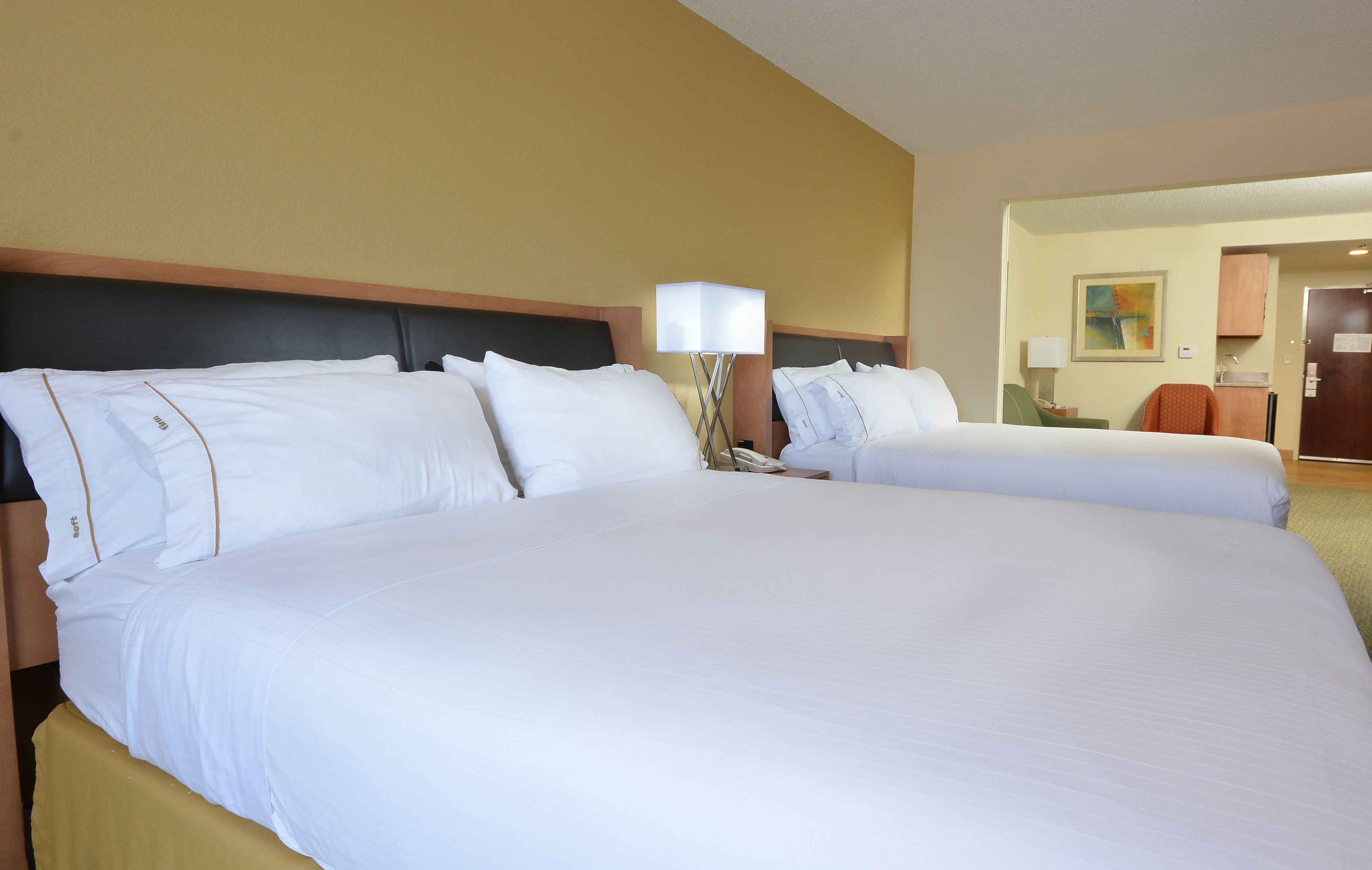 A hotel room with two large beds, a bedside table with a lamp, and a door leading to a bathroom.