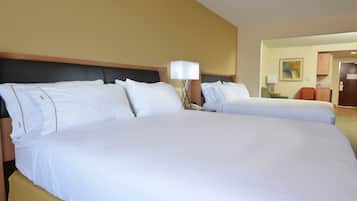 A hotel room with two large beds, a bedside table with a lamp, and a door leading to a bathroom.