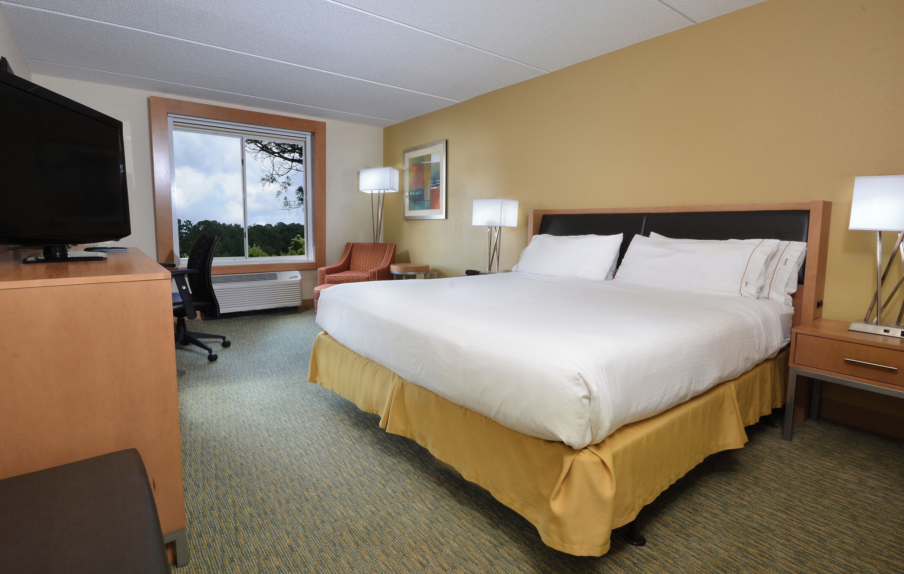 A hotel room with a large bed, a desk, a chair, a television, and a window with a view of trees.