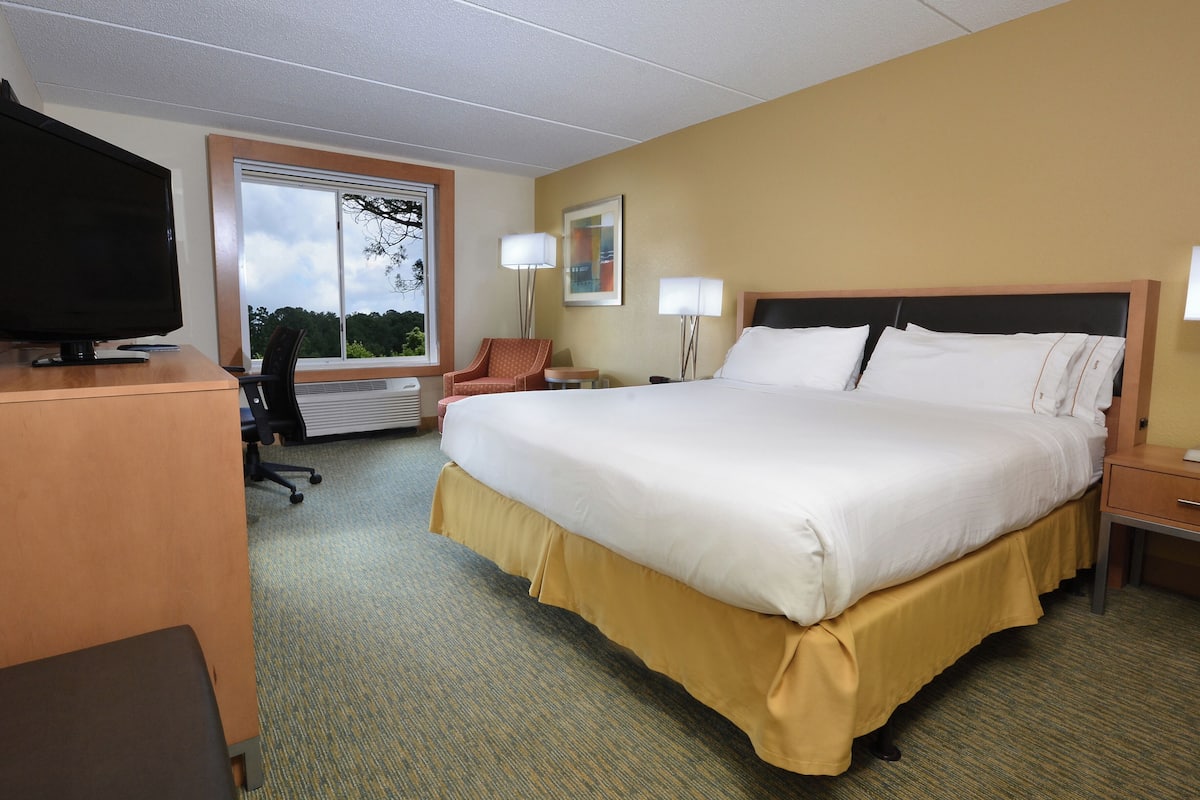 A hotel room with a large bed, a desk with a TV, a chair, and two bedside lamps.
