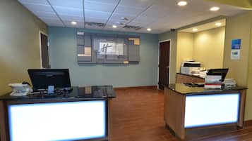 A hotel reception desk with a computer, a printer, and a sign indicating the hotel name.