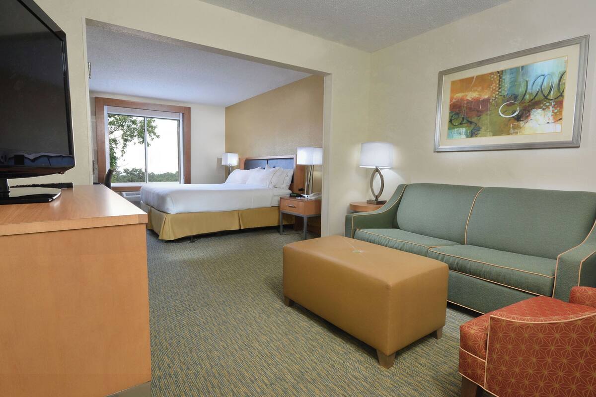 A hotel room with a bed, a desk, a television, a sofa, and a painting on the wall.