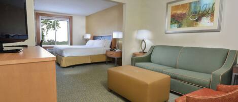 A hotel room with a bed, a desk, a television, a couch, an ottoman, and a painting on the wall.