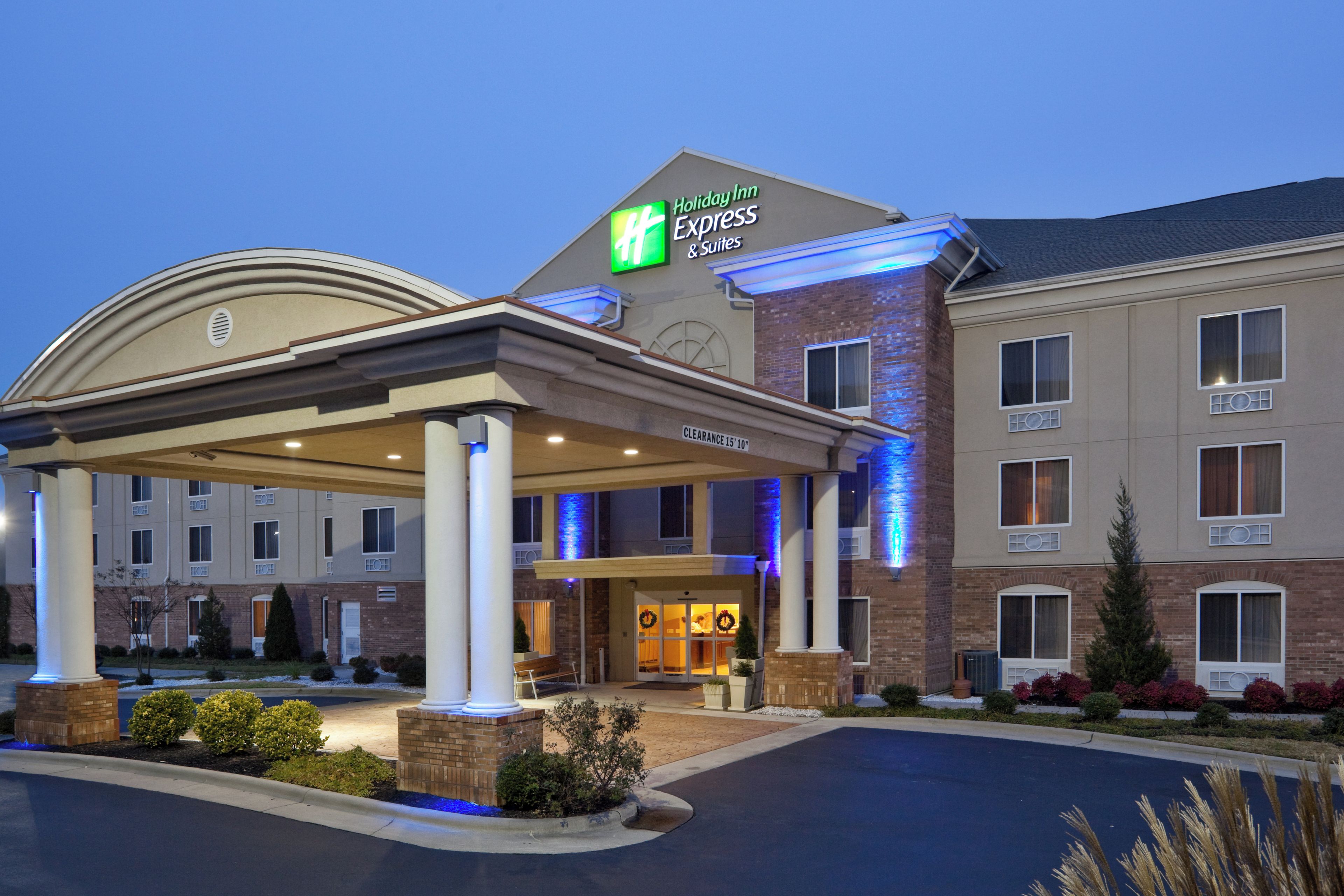 A Holiday Inn Express & Suites hotel with a covered entrance, a brick facade, and a clear sky.