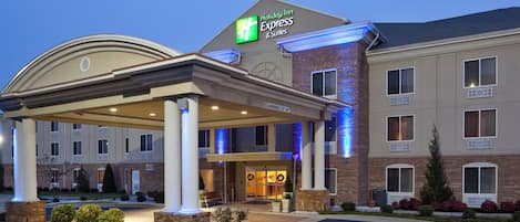 A Holiday Inn Express & Suites hotel with a covered entrance, a brick facade, and a clear sky.