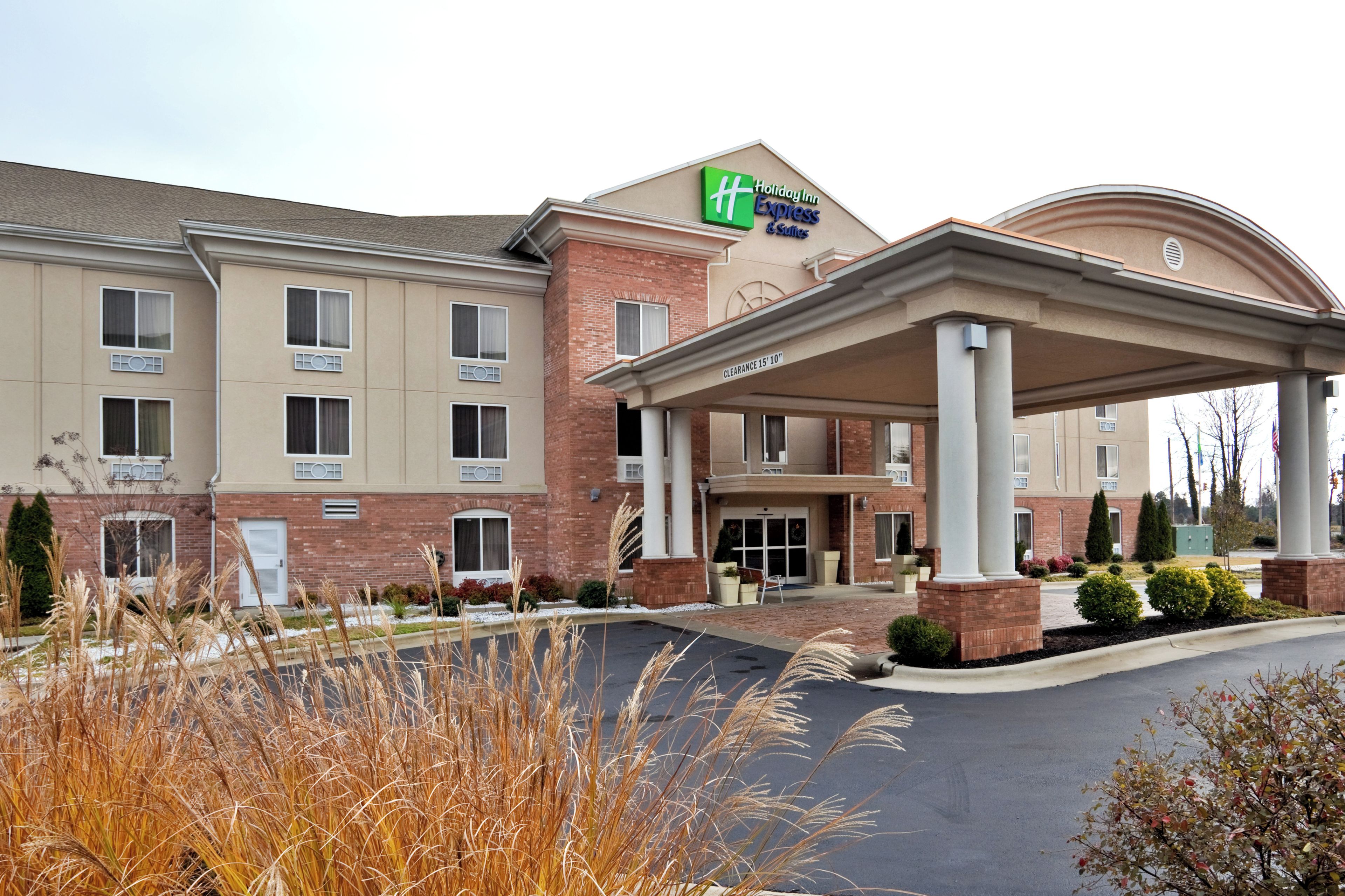 Ein Holiday Inn Express & Suites Gebäude mit überdachter Einfahrt, einer Ziegel-Fassade und einem deutlichen Schild mit dem Hotelnamen.