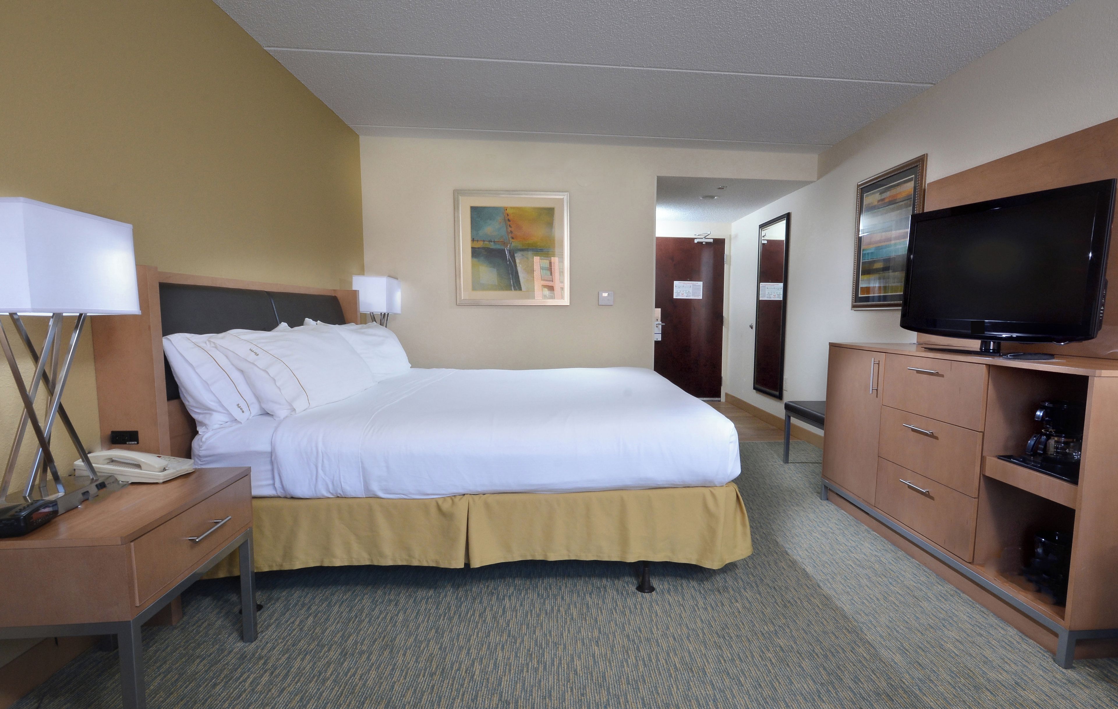 Habitación de hotel con una cama, un escritorio con teléfono, televisor y un mueble con cajones.