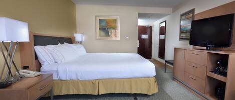 Habitación de hotel con una cama, un escritorio con teléfono, televisor y un mueble con cajones.
